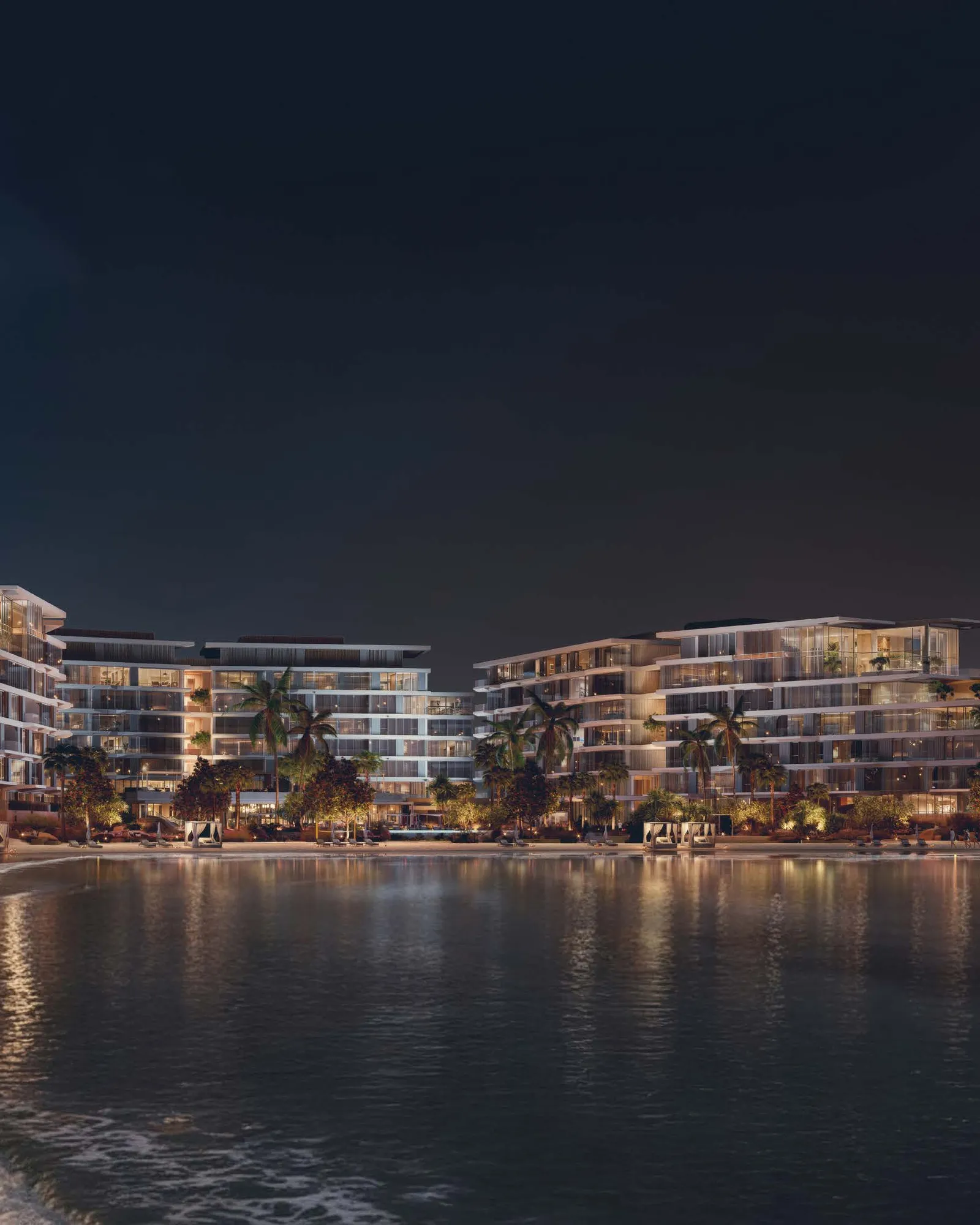 The buildings lit at night, reflected in the water off the private beach